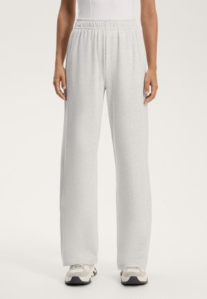 Hellgraue Sweatpants mit lockerem Schnitt, elastischem Bund und weicher Textur. Kombiniert mit neutralen Sportschuhen.