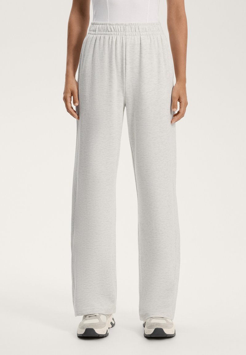 Svetlo sivi trenirka s sproščenim krojem, elastičnim pasom in mehkimi vlakni. V kombinaciji z športnimi čevlji nevtralnih tonov.