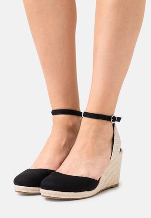 Chaussures compensées en tissu noir avec un talon tressé beige texturé et une bride de cheville ornée d'une boucle en argent.