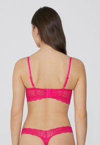 Kanten bralette in een levendige roze kleur met verstelbare bandjes, golvende randen en haaksluiting. Bijpassende kanten string inbegrepen.