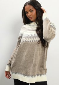 Maglione lavorato a maglia beige con colletto alto, caratterizzato da un motivo geometrico bianco e grigio. Vestibilità ampia e maniche lunghe, texture morbida.