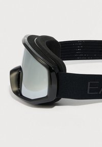 Μαύρα γυαλιά σκι με αντανακλαστικούς ασημένιους φακούς και επένδυση αφρώδους μαξιλαριού, με ρυθμιζόμενο μαύρο ελαστικό λουράκι με υφή για καλύτερη πρόσφυση.