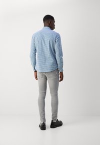 Light blue checked shirt with a collar, buttoned cuffs, and a curved hem, paired with gray slim-fit jeans and black shoes.