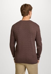 Brązowy sweter z dzianiny warkoczowej z okrągłym dekoltem, ściągaczami na mankietach i na dole. Posiada fakturowane pionowe wzory i luźny krój.