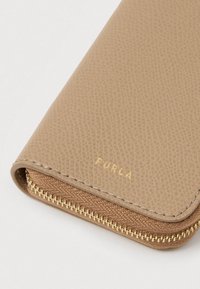 Beige tekstureret læderpung med guldfarvet hardware, der har en lynlåslukning og et præget logo på forsiden. Glat og holdbart finish.