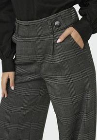 Grau kariierte Hose mit hohem Taillenbund, ausgestattet mit einem schwarzen Knopf, Seitentaschen und einer Mischung aus Hahnentritt- und Linienmustern.