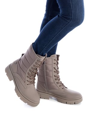 Bottes en dentelle couleur tan avec des panneaux latéraux matelassés, des semelles en caoutchouc texturé et un bout arrondi. Conçues pour le confort et la durabilité.