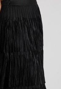 Falda negra plisada con textura en capas, que presenta pliegues verticales, una cinturilla ancha y un acabado de tejido suave.