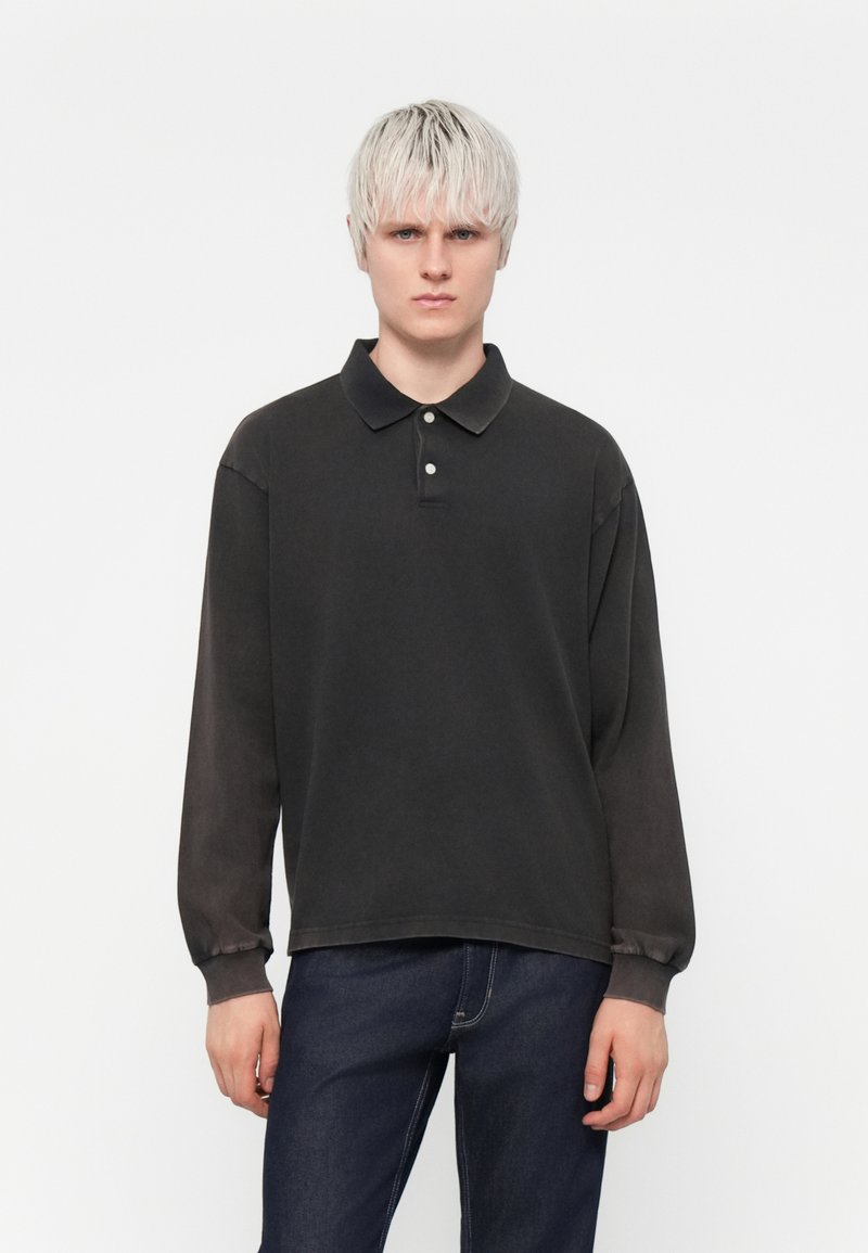Schwarzes Langarm-Polohemd mit Kragen, aus weichem Material, mit drei Knöpfen; getragen mit dunklen Jeans.