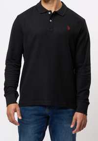 Polo shirt nero a maniche lunghe con colletto classico, placca a tre bottoni e piccolo logo rosso sul petto, realizzato in tessuto testurizzato.
