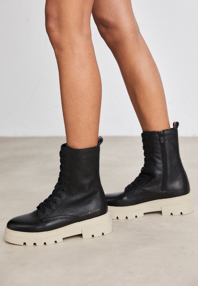 Bottines en cuir noir à finition texturée, semelle beige épaisse, fermeture à lacets à l'avant et zip latéral pour un accès facile.