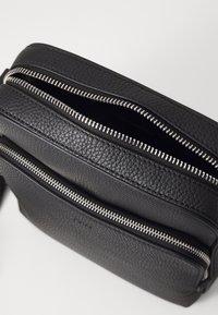 Svart läder crossbody-väska med två zip-fack, med texturerad yta och silverfärgade metalldragkedjor. Kompakt och funktionell design.