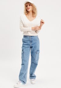 Hvid og beige stribet langærmet bluse med V-udskæring, parret med lyseblå cargobukser med store sidelommer.
