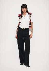 Jeans noirs à jambes larges associés à un haut blanc à manches courtes côtelé et un gilet en maille à rayures multicolores aux tons rouges, gris et marron.