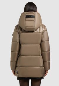 Pufferjack in taupe kleur met een gestructureerde capuchon, geborduurd ontwerp en een logo patch op de rug. Heeft lange mouwen en een slim fit.