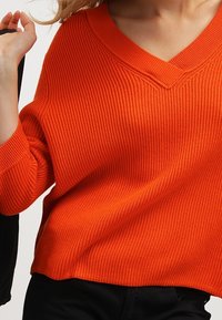 Ripp Pullover in Orange mit V-Ausschnitt und lässiger Passform. Hergestellt aus einem strukturierten Strickstoff, mit fallenden Schultern und ärmellangen Ärmeln.