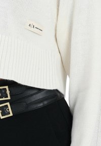 Maglione bianco corto lavorato a maglia con orlo a costine, con etichetta A|X Armani Exchange. Abbinato a una cintura a vita alta nera con fibbia.