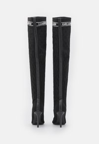 Bottes noires en tricot, montant jusqu'aux genoux, avec un motif texturé, dotées d'accents en cuir élégant et de talons aiguilles. Bande logo en haut.