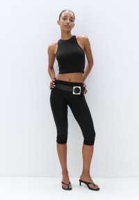 Svart crop top med hög halsringning, ihopparad med åtsittande svarta capri leggings och ett brett svart bälte med en silverspänne. Svarta flip-flops.