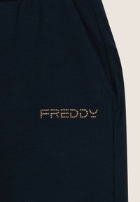 Pantalón jogger de azul marino oscuro con textura suave, que presenta el logo "FREDDY" en tachuelas doradas en el lado izquierdo. Incluye bolsillos laterales y cintura elástica.