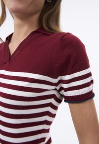 Polo a maniche corte a righe bordeaux e bianche con scollatura a V e rifiniture blu navy ai polsini, realizzato in un morbido materiale a maglia.