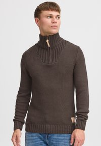 Brun strikket sweater med høj ribbet krave og lynlås halvvejs ned. Har et tekstureret mønster samt ribbede manchetter og kant.