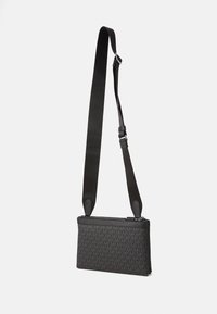 Black crossbody bag featuring a zip closure, patterned exterior, and an adjustable strap made of smooth material with a matte finish.