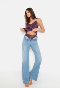 Fialový pruhovaný crop top a zodpovedajúce bikiny, doplnené o voľné, svetlo modré džíny, nosené nezošité. Viditeľné holé nohy.
