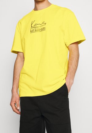 Camiseta de algodón amarilla con mangas cortas, con una impresión de logotipo negro en el pecho. Cuello redondo y corte relajado, textura suave.