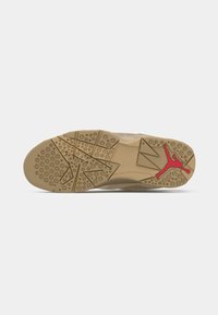 Semelle de sneaker beige avec un motif texturé. Présente des grips circulaires et un logo Jumpman rouge en contraste. Matériau en caoutchouc durable.