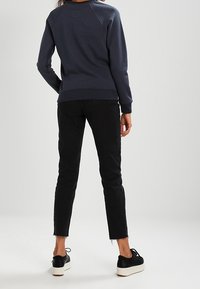 Sudadera de cuello redondo en color navy con puños de canalé, combinada con jeans skinny negros con dobladillos deshilachados y zapatillas negras con suelas blancas.