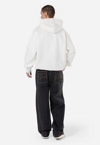 White oversized hoodie, dark loose-fitting jeans with unique pocket design, and sneakers, viewed from the back.