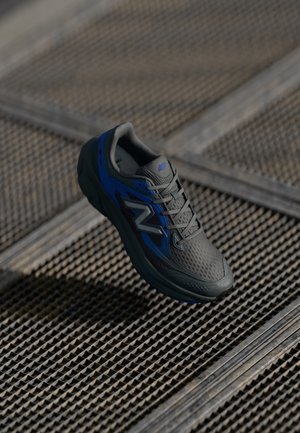 Baskets de sport grises avec des accents bleus, dessus en mesh respirant, semelle texturée et éléments réfléchissants, présentant un design léger.