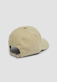 Beige cotton cap with a curved brim, textured fabric, six-panel design, adjustable strap at the back, and ventilation eyelets.