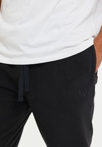 Zwarte fleece joggers met een elastische tailleband en trekkoord, voorzien van zijzakken en een subtiele logo in een tonale zwarte print.