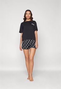T-shirt en coton noir avec le logo "HUGO", associé à un short noir et blanc à motifs présentant un design géométrique.
