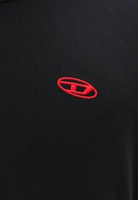 T-shirt noire en coton, avec un logo rouge brodé au centre, un col rond et des manches courtes.