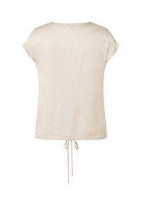 Blouse à manches courtes en tissu beige doux, avec une coupe décontractée et un détail de lien ajustable à l'arrière. Texture lisse sans motifs.