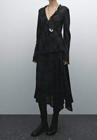 Robe à carreaux noire et bleu marine avec des bords effilochés, manches longues et décolleté en V, accompagnée d'une longue jupe fluide et de bottines ajustées.