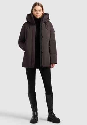 Dunkelgraue Puffjacke mit Kapuze, ausgestattet mit einem Reißverschluss und Knöpfen, aus glattem Stoff. Trägt man über schwarzen Leggings und knielangen Stiefeln.