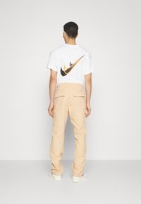 White t-shirt with a black and orange Nike logo on the back, paired with light beige cargo pants featuring side pockets.