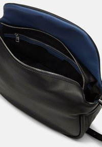 Schwarze Lederhandtasche mit Reißverschluss, ausgestattet mit einem blauen Stofffutter und einer Innentasche. Glatte Textur und minimalistische Designelemente sind sichtbar.