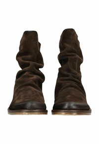 Bruine suède enkellaarsjes met een slordig ontwerp en zwarte leren neuskapjes; platte zool, zachte textuur en minimale details.