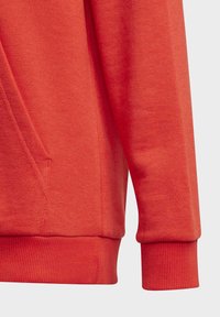 Felpa rossa con una texture morbida, polsini a costine e una tasca laterale. Presenta un design pulito con dettagli di cuciture minimaliste.