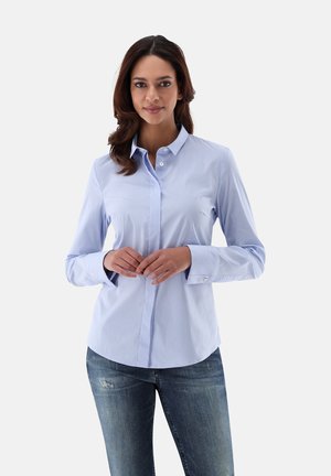 Light blue striped button-up shirt with a pointed collar, long sleeves, and single-button cuffs, paired with fitted dark jeans.