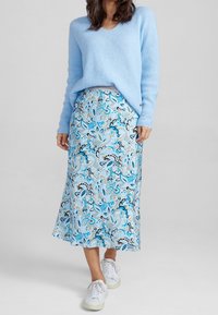 Hellblauer, strukturierter Pullover kombiniert mit einem knielangen Rock mit einem blau-weißen Paisley-Muster. Vervollständigt mit weißen Turnschuhen.