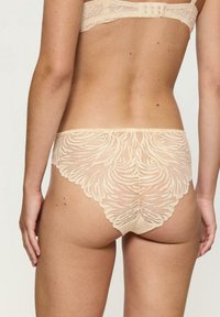 Beżowa koronkowa bielizna z kwiatowym wzorem, z falbankami i gładką, miękką podszewką zapewniającą komfort. Wyświetlony widok z tyłu.