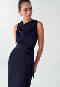 Marineblaues ärmelloses Kleid mit einem drapierten Ausschnitt und einer gebundenen Taille. Glatte Textur mit einer figurbetonten Silhouette und einem fließenden Rock.