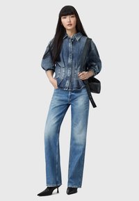 Giacca di jeans con un design aderente e maniche a sbuffo abbinata a jeans dritti azzurri e décolleté nere a punta. Borsa a spalla nera.