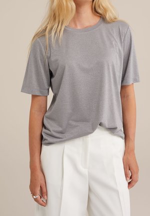 Grå kortærmet t-shirt med en subtil glans, med løstsiddende pasform og rund halsudskæring, parret med hvide skræddersyede bukser.